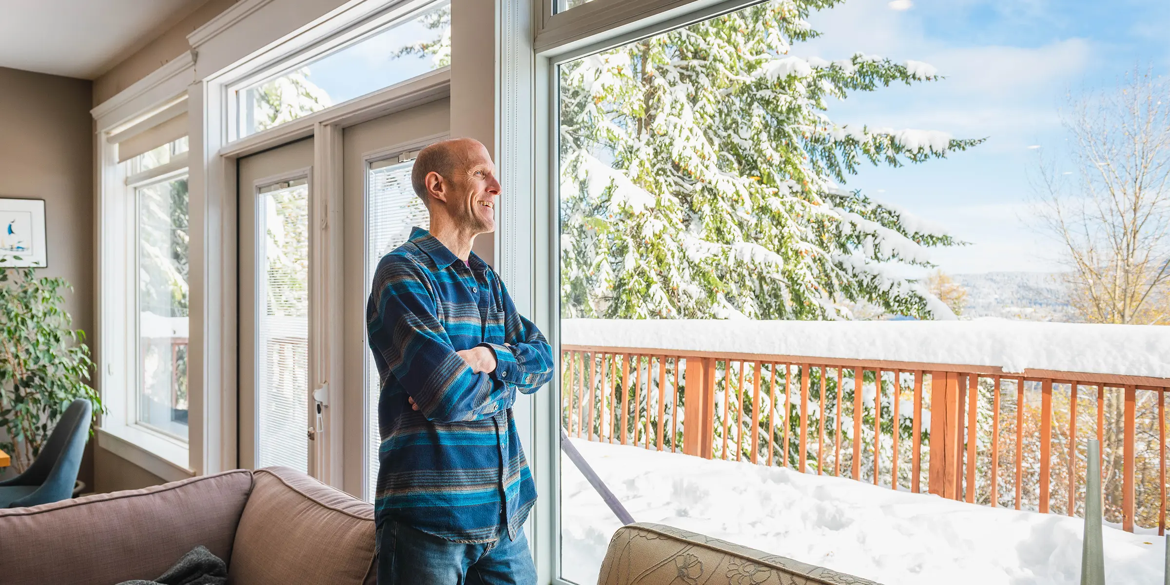 Man gazes out window onto snow covered deck.