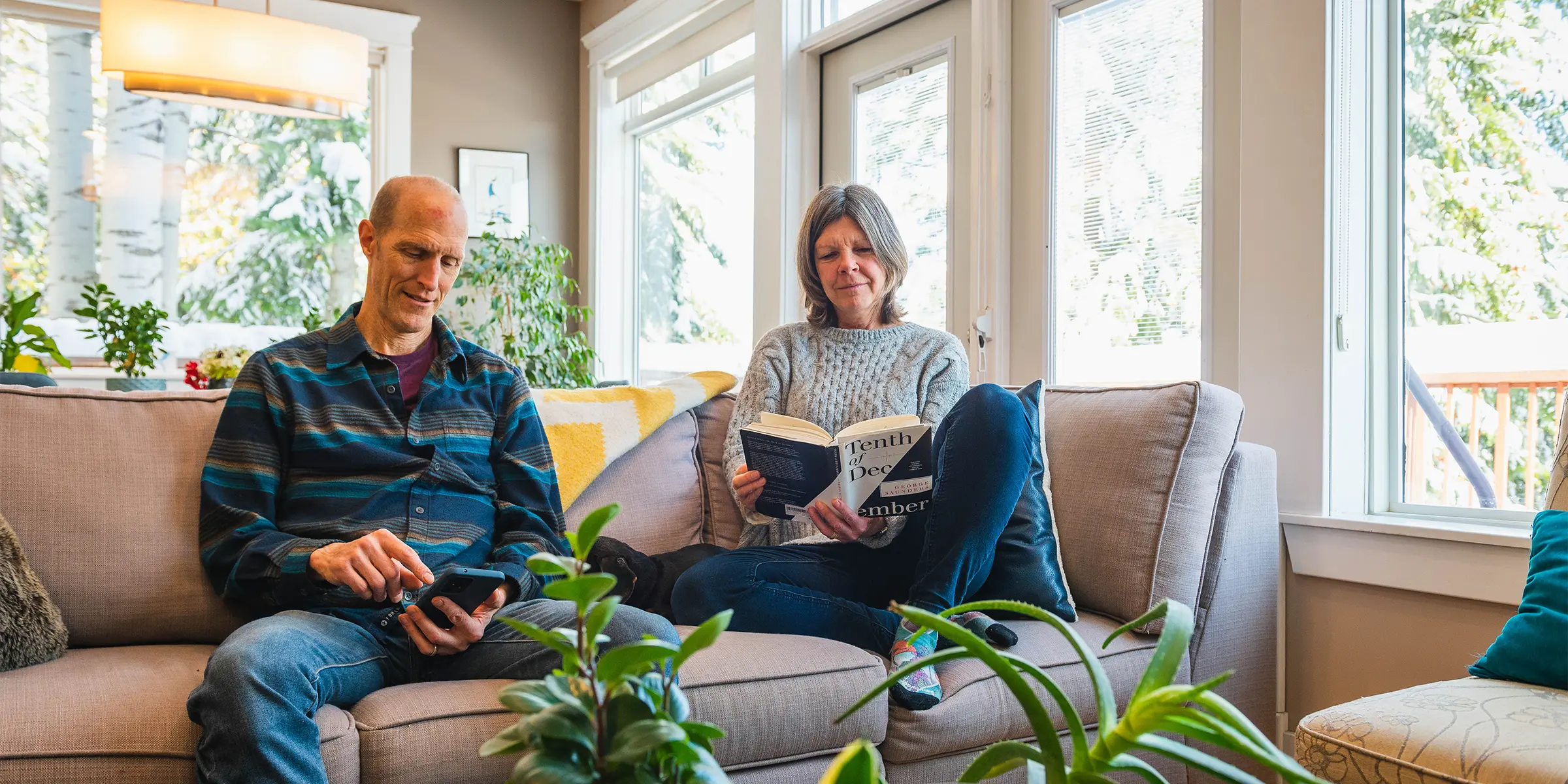 Man and woman reading books on sofa in sunlit living room.